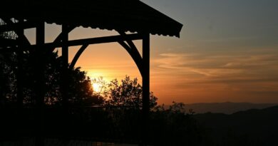 A wooden gazebo silhouette against a warm orange sky and distant mountain ridges